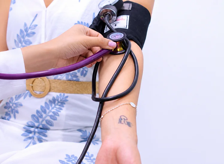 Primer plano de un profesional de la salud midiendo la presión arterial de un paciente utilizando un estetoscopio y un brazalete de presión arterial.